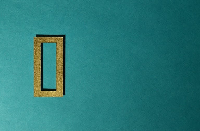 A gold rectangular frame casting a shadow on a teal background, minimal and artistic.