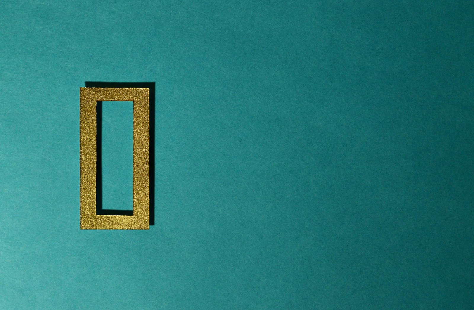 A gold rectangular frame casting a shadow on a teal background, minimal and artistic.